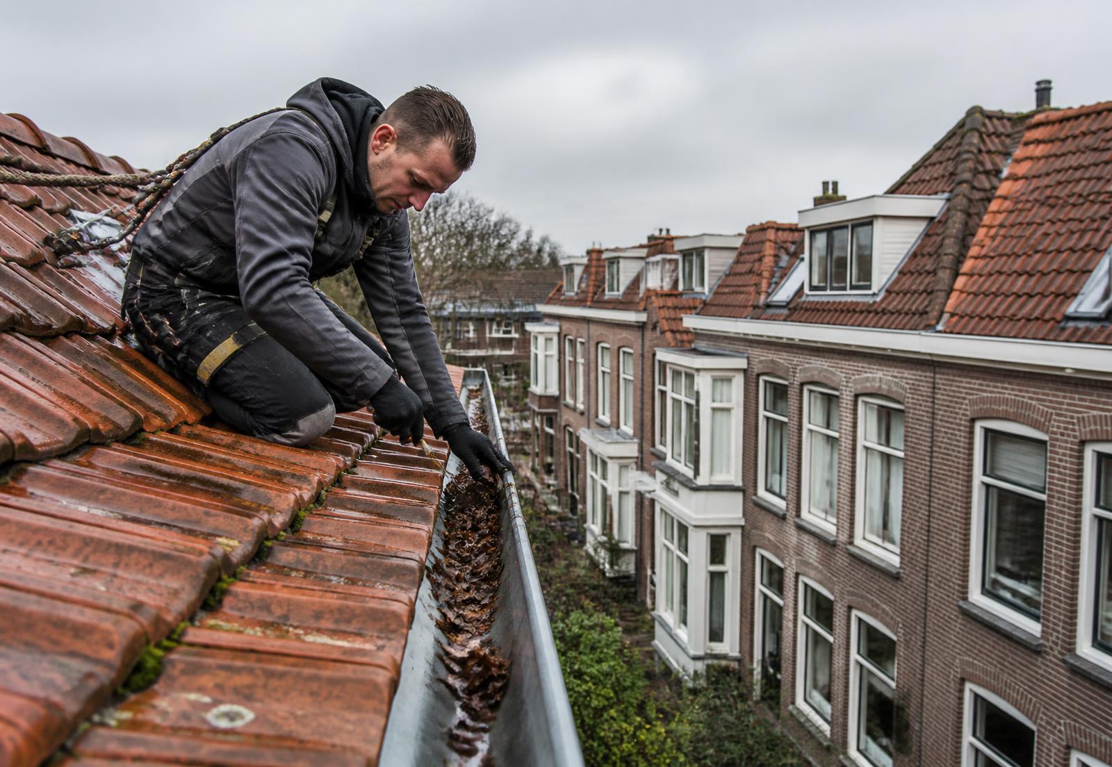 Dakdekker verwijdert bladeren uit de zinken dakgoot van een pannendak tijdens dakonderhoud