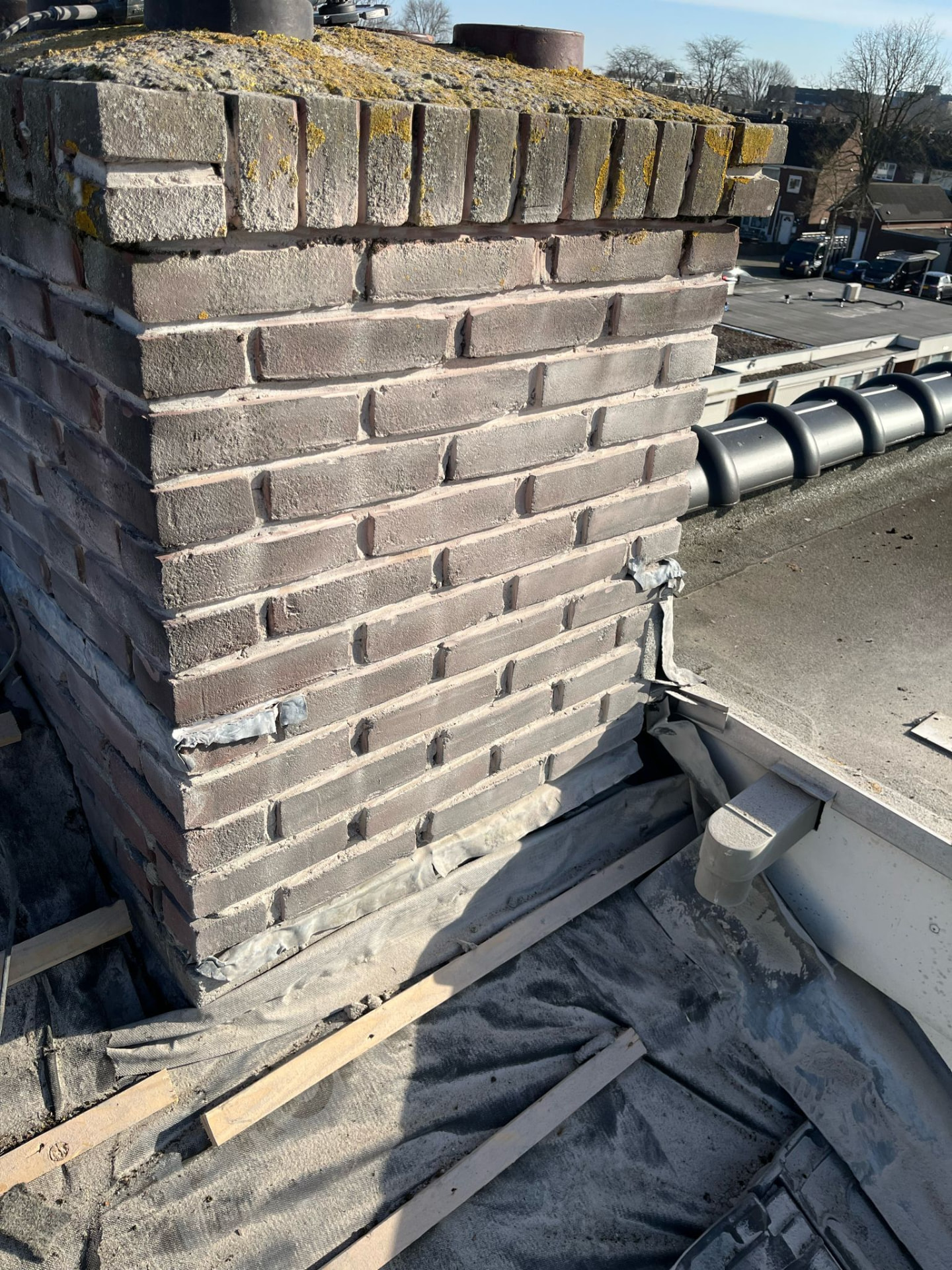Dakreparatie aan een gemetselde schoorsteen met herstel van voegwerk en loodaansluiting op een plat dak