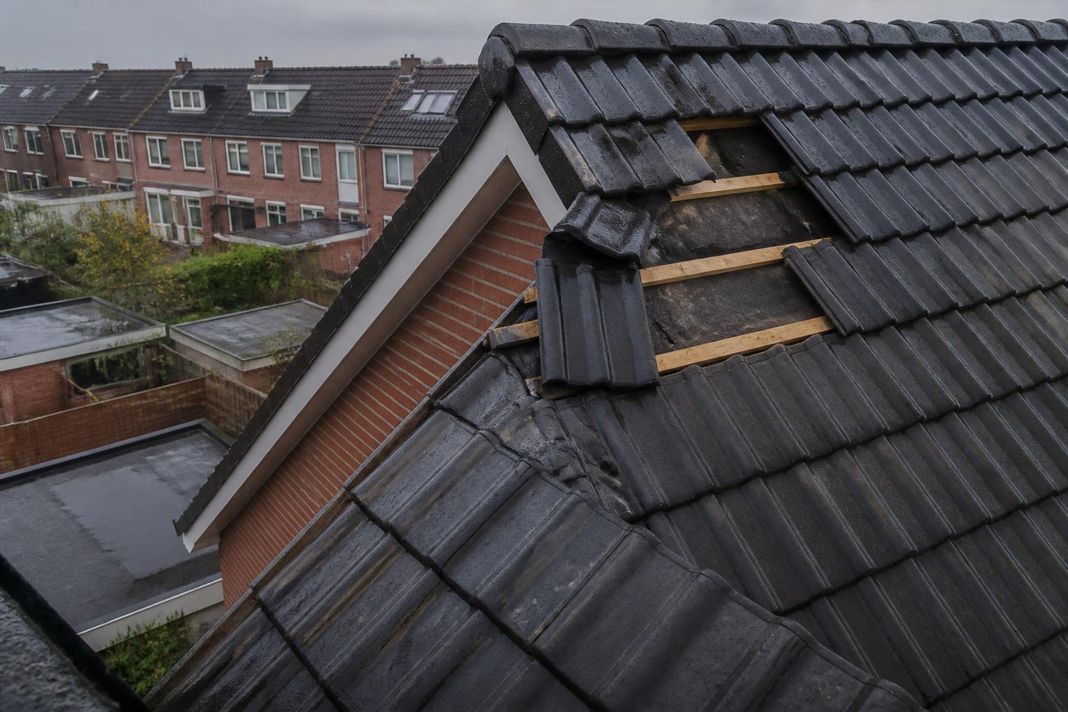 Verschoven en weggewaaide dakpannen op een pannendak na een storm, met zichtbare panlatten