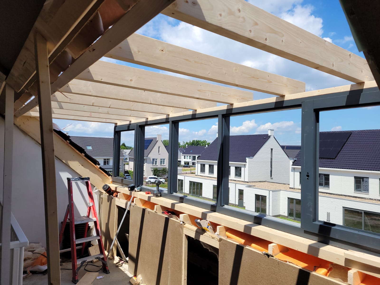 Nieuwe dakkapel in aanbouw met houten dakbalken en antracietkleurige kozijnen op een zolderverdieping