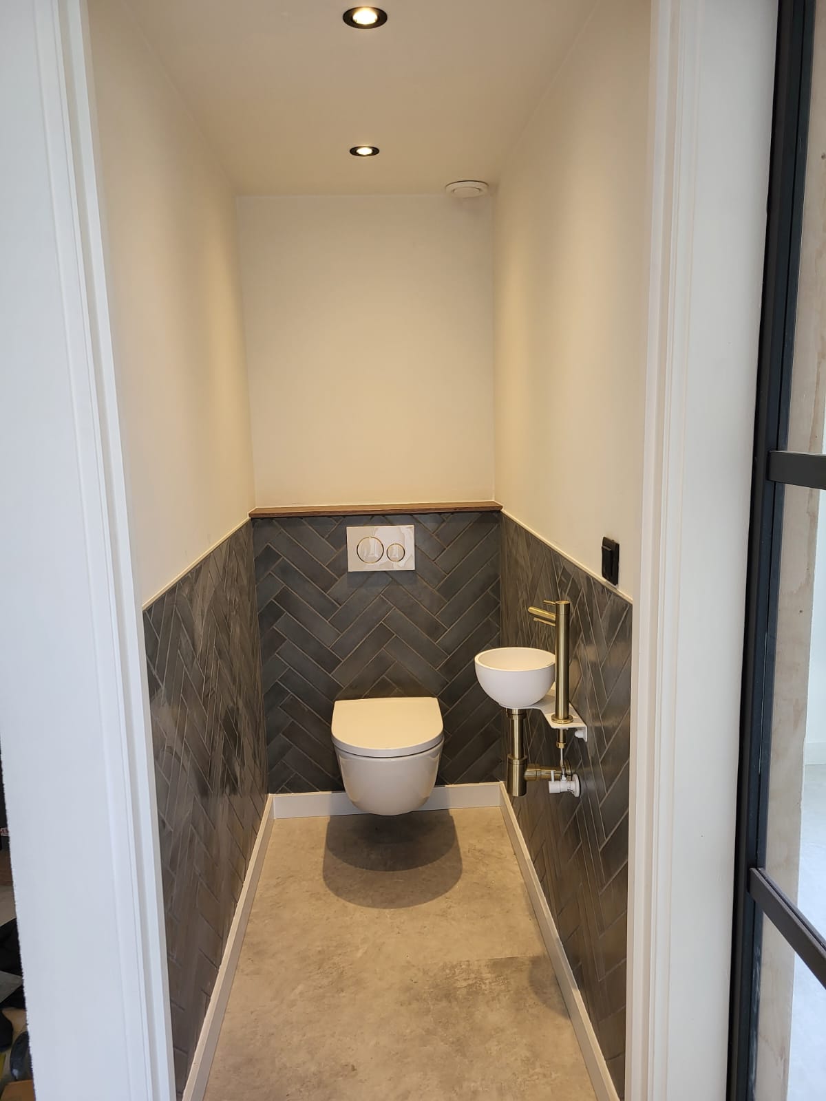 Gerenoveerd toilet met visgraat wandtegels, houten afdeklat en zwevend fonteintje