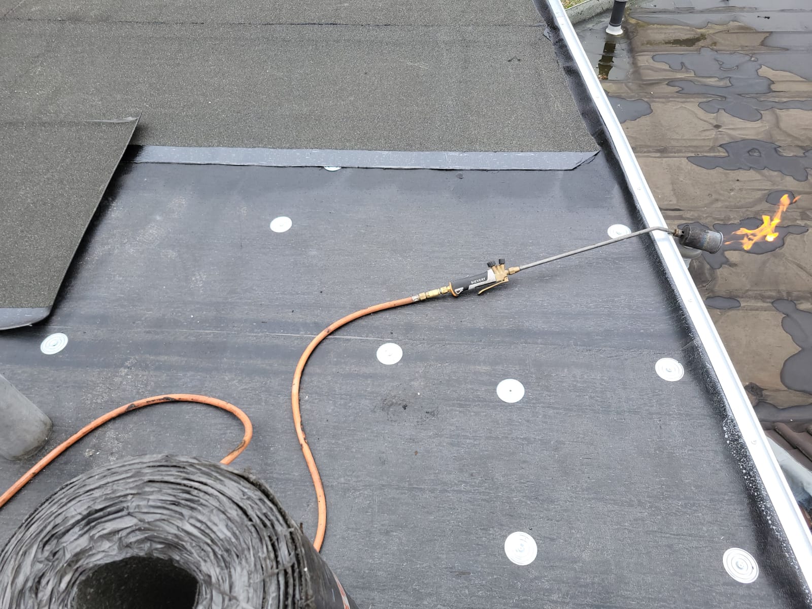 Plat dak met EPDM-dakbedekking dat met een brander en dakrol wordt afgewerkt langs de aluminium daktrim
