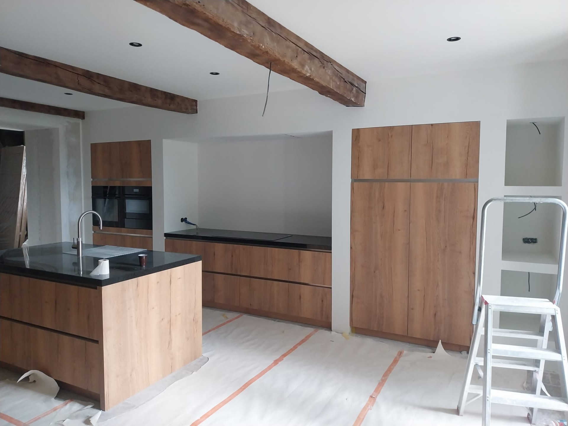 Afgetimmerde keukenwand met eiken kastenwand, koof en strakke aansluitingen op de balken tijdens de afwerkfase